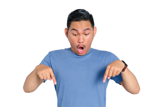 Surprised young Asian man pointing down with both hands, wearing casual blue t-shirt, isolated on transparent background - Powered by Adobe