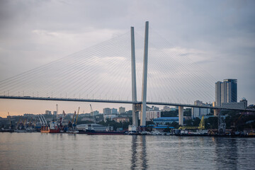 Obraz premium Cable stayed bridge spanning golden horn bay, with bustling port and cityscape of vladivostok in the background, during a vibrant sunset
