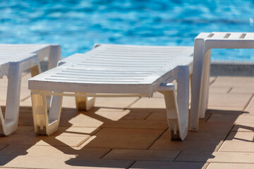 A white lounge chair is sitting on a tan brick patio next to a pool