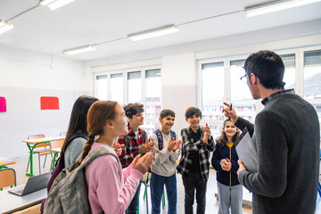 Group of happy elementary school students clapping hands in classroom while learning with their teacher