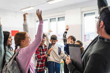 Cheerful students raising hands enthusiastically while answering their teacher's question in a...