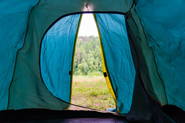Tent interior framing verdant forest meadow, sunlight filtering through open canvas revealing lush...