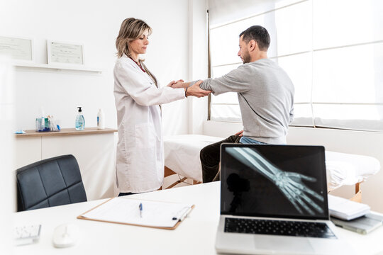 Doctor examining patient's arm in a medical clinic with x-ray on screen