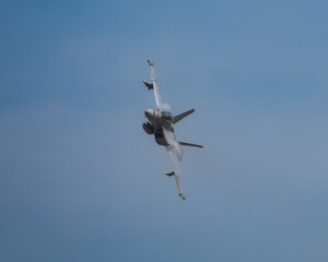 Military jet aircraft performing a tight banking turn, creating vapor trails in the clear sky.