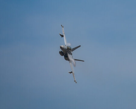 Military jet aircraft performing a tight banking turn, creating vapor trails in the clear sky. - Powered by Adobe