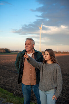 Grandfather and granddaughter in a field with a wind turbine in the background