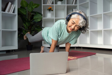 Senior Fitness and Online Training. An elderly woman exercising at home, engaged in a workout via laptop.