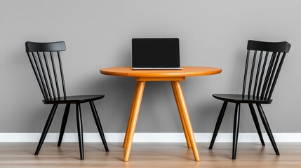 Fototapeta premium Laptop on a small wooden table between two black chairs against a gray wall.