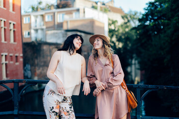 Naklejka premium Two smiling women leaning on a bridge railing in a european city