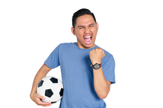 Excited young Asian man celebrating victory, holding soccer ball and showing fist pump, isolated on transparent background