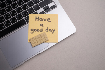 Piece of paper with the inscription Have a good day and a piece of chocolate on the table. Warm wishes