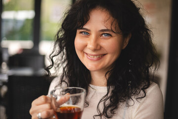 Happy brunette curly woman sitting in cafe and enjoy of smell and taste of tea, when have good...