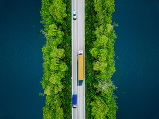 Aerial view of heavy truck and cars on asphalt road over blue water lake