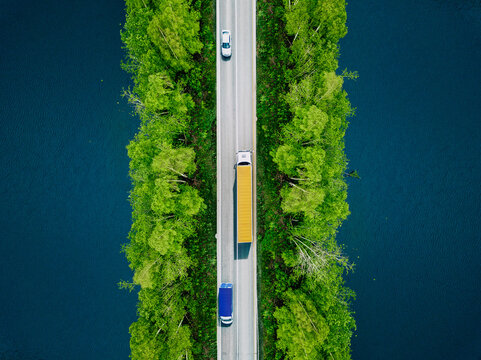 Aerial view of heavy truck and cars on asphalt road over blue water lake