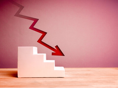 Crisis chart and graph. Economic downturn with decrease arrow on white empty steps as graph on wood table, red background with copy space. Business volatility trend process, financial concept.