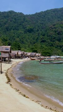 Nestled along a serene shoreline, traditional wooden huts blend seamlessly with lush greenery and clear turquoise waters of Koh Surin Thailand
