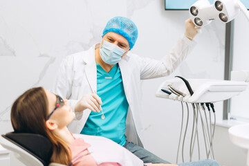 Obraz premium Male stomatologist in uniform taking visional inspection of woman on the chair in dental clinic