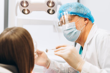 Naklejka premium Young woman undergoing treatment at dental clinic, doctor wearing protective mask