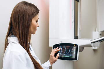 Portrait of woman in a medical coat adjusting a dental tomograph