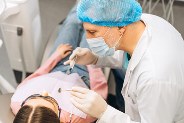 Portrait of male dentist in protective face mask treating teeth of female patent