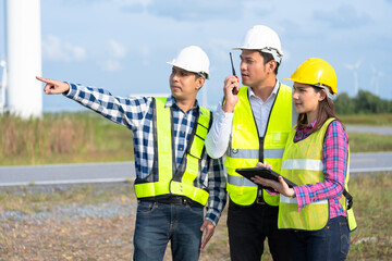Three engineers collaborating in the wind power business while adhering to industry standards, using a tablet to monitor performance and strategize on future energy development.