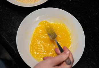 Female hands beat eggs with fork in a bowl, homemade schnitzel cooking process closeup