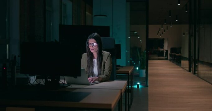 Female businesswoman employee working late in the office, using a laptop while feeling tired and burnt out. Reading, copywriting, editing, and struggling with fatigue and brain fog on a tight deadline