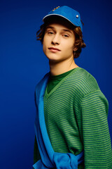 Young man showcases trendy fashion in vibrant setting with striking blue backdrop