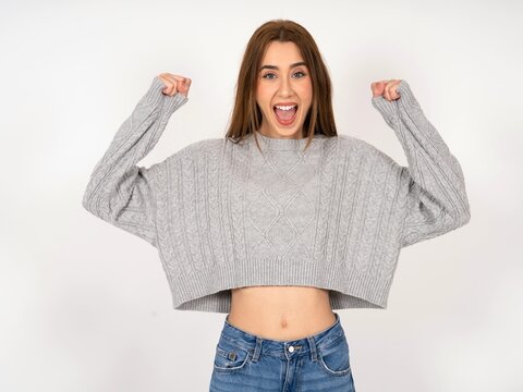 Shocked ecstatic Caucasian young girl wearing grey sweater win luck lottery raise hands up shout yea