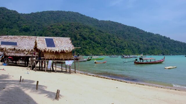 Warm sunshine illuminates the sandy beach in Koh SurinThailand, highlighting traditional bamboo huts and vibrant fishing boats.
