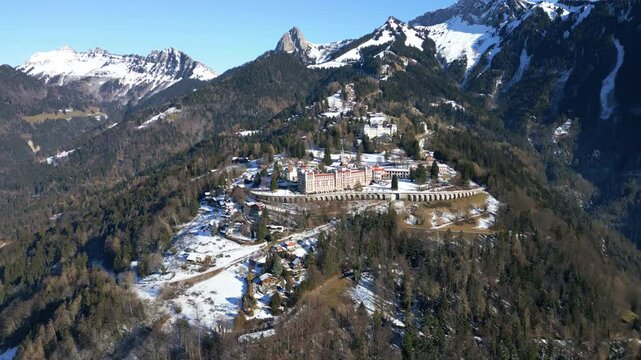 Parallax drone shot from afar of Caux Palace Hotel with snow during the day in the village of Caux, canton of Vaud, Switzerland