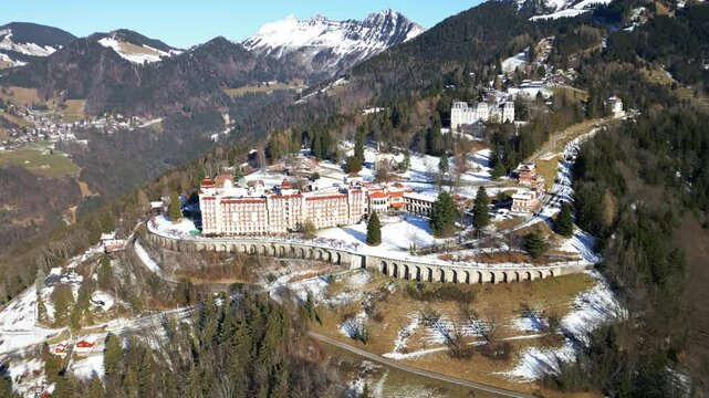Aerial: Caux Palace Hotel with snow during the day in the village of Caux, canton of Vaud, Switzerland, parallax drone shot