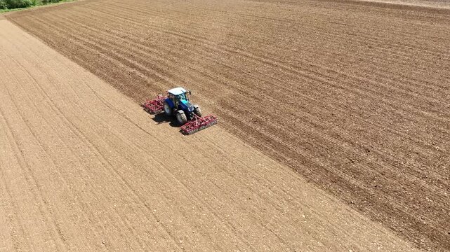 Un tracteur laboure et herse un champ avant la semence