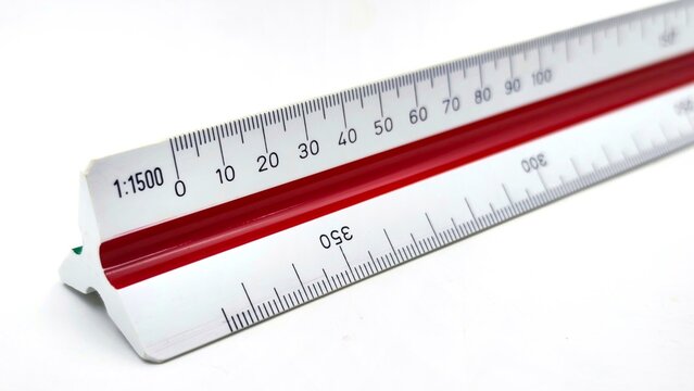 Closeup view of a triangular scale ruler with multiple measurement scales, including 1:1500, featuring red central groove for architectural and engineering drafting, isolated on white background.