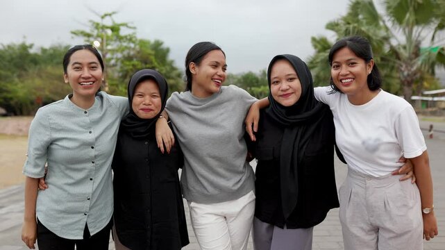 Portrait of diverse young asian girls smiling at camera standing together outdoors. Youth community and female friendship concept with happy gen z student women hugging each other at city street. 