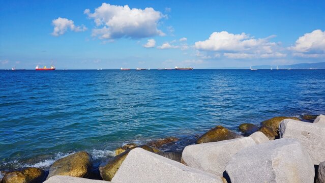 Peaceful seaside view with clear blue waters, rocky coast and a few boats in the distance.