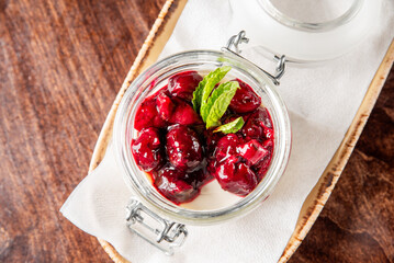 A delicious jar of creamy panna cotta topped with vibrant berry compote and a sprig of mint, elegantly presented on a tray with a folded napkin against a wooden background.