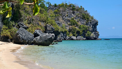 Secluded Tropical Beach with Crystal Clear Water and Rocky Cliffs Covered in Greenery Under Bright Blue Sky