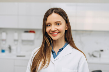 Happy young female dentist wearing uniform posing at camera in her office
