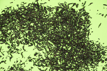 Scattered leaves of black large leaf tea on green background top view