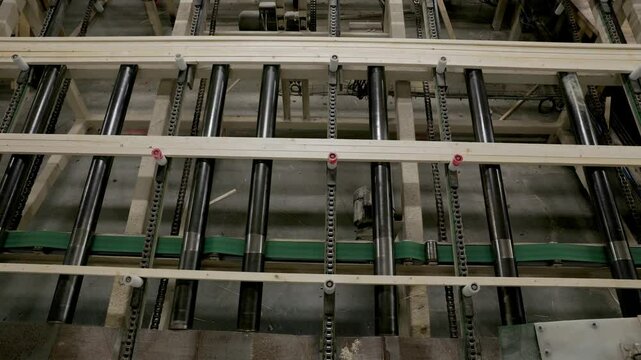 Top-down view of wooden planks on a powered roller conveyor with chains, showing an automated system used for transporting processed timber in an industrial facility
