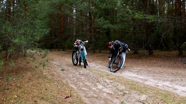 Two cyclists encounter a flat tire while exploring a forest path during a cloudy day