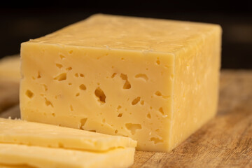cheese with holes for cooking, pieces of sliced cheese on a cutting board, side view