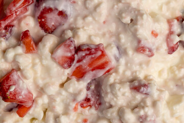 cottage cheese with sour cream and fresh red strawberries, white sour-milk cottage cheese with strawberries cut into pieces, closeup