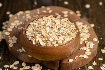 wooden bowl with oatmeal flakes for making porridge, scattered dry cereal flakes from oats flattened and steamed, closeup