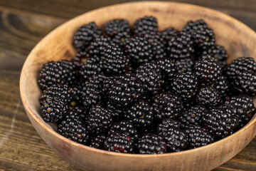 black blackberries in a wooden bowl, sour but ripe blackberries on the table, side view