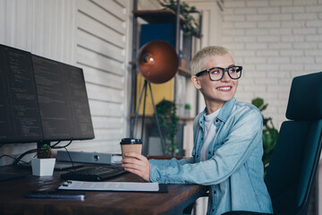 Young professional woman sipping coffee at workstation with dual monitors