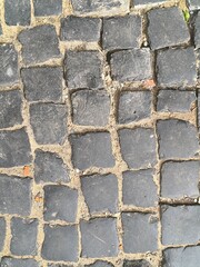 Close-up of a cobblestone pavement with uneven dark stones and sandy joints. The aged, rustic texture is ideal for use in architectural designs, backgrounds, and street-themed visuals