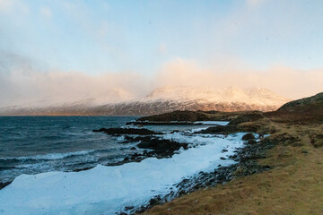 An ice-clad beach in the Icelandic winter, near Djupivogur, showing the black lava beaches along the Berufjordir, while the low sun casts an orange glow along the horizon.