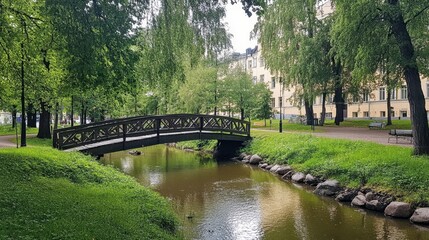 Obraz premium A lush green park in Helsinki with a wooden bridge crossing over a small river.
